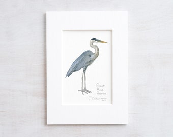 Puede incluir: Una pintura de acuarela enmarcada de una garza azul, una ave zancuda alta con plumas grises y un pico largo y delgado. La pintura está firmada "Christopher 2019".