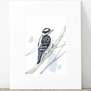 May include: Watercolor painting of a black and white woodpecker with a red crown perched on a branch. The background is a light blue watercolor wash.