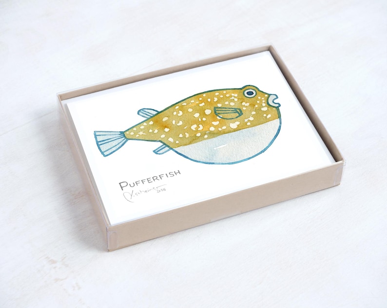 May include: A set of cards featuring a watercolor illustration of a pufferfish. The fish is yellow with white spots and blue accents, and is contained in a light brown box. The text "Pufferfish" and an artist's signature are visible.