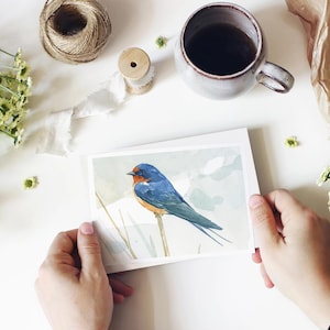 May include: A watercolour painting of a bluebird perched on a branch. The bird has a blue body, a brown head, and a long tail. The background is a soft, watercolour wash of blue and green.