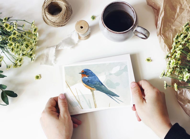 May include: A watercolour painting of a bluebird perched on a branch. The bird has a blue body, a brown head, and a long tail. The background is a soft, watercolour wash of blue and green.