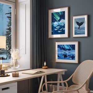May include: Three framed illustrations of whales and the aurora borealis in a home office setting. The illustrations are in shades of blue and green, with a white background. The illustrations are hanging on a dark blue wall, above a white desk with a wooden chair.