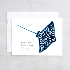 May include: A watercolor illustration of a spotted eagle ray in shades of blue and white. The image is on a white card with the text "Spotted Eagle Ray" and a signature. The card is inside a white envelope.