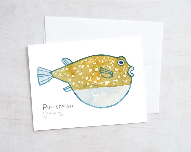 May include: Watercolor illustration of a pufferfish on a white card. The fish is yellow-brown with white spots and blue fins. The card is paired with a white envelope. The word "Pufferfish" is written below the fish.