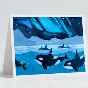 May include: Watercolor painting of a pod of orcas swimming in the ocean under a blue and green aurora borealis. The orcas are black and white and the water is a deep blue.