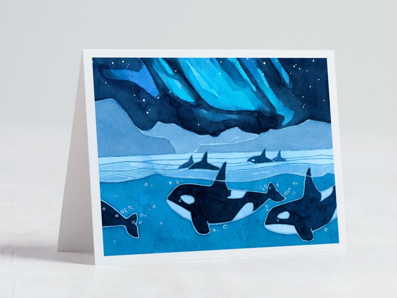 May include: Watercolor painting of a pod of orcas swimming in the ocean under a blue and green aurora borealis. The orcas are black and white and the water is a deep blue.