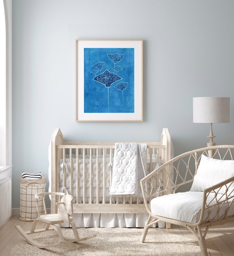 May include: A white wooden rocking horse in a nursery setting with a crib, a wicker chair, and a framed print of blue stingrays on a blue background.