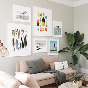 May include: A living room with a light beige sectional sofa, two throw pillows, a throw blanket, and a round woven coffee table. The wall behind the sofa is decorated with a gallery wall of framed prints featuring birds, feathers, and buoys. A potted plant is in the corner of the room.
