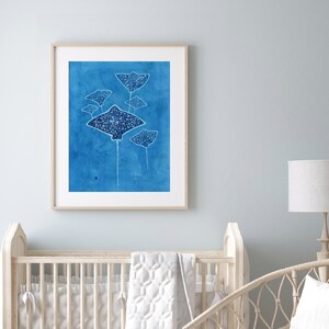 May include: A framed watercolor painting of a group of stingrays swimming in a blue ocean. The stingrays are white with black spots and are silhouetted against the blue background.