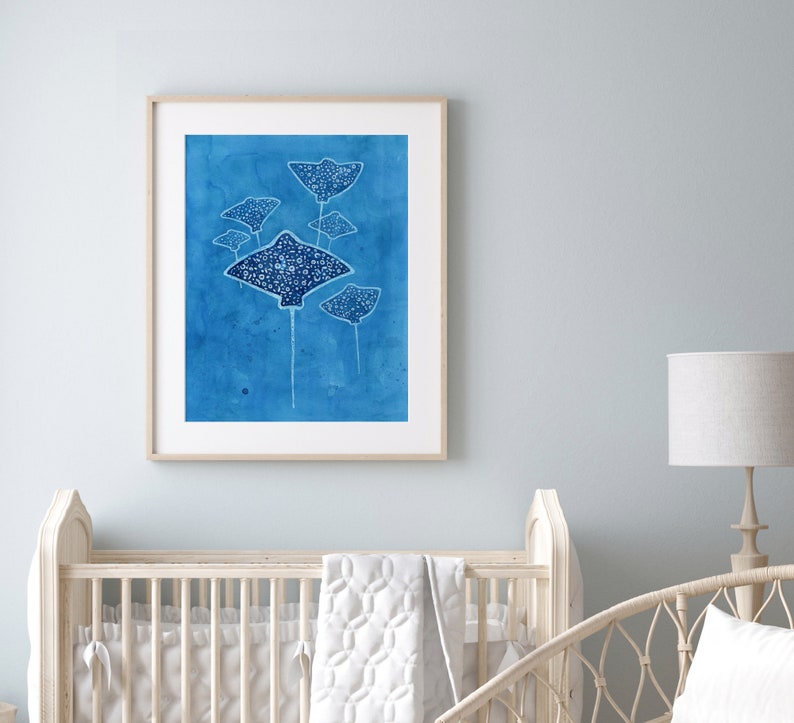 May include: A framed watercolor painting of a group of stingrays swimming in a blue ocean. The stingrays are white with black spots and are silhouetted against the blue background.