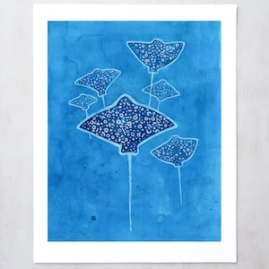 May include: A watercolor painting of five stingrays swimming in a blue ocean. The stingrays are white with black spots and have long tails.