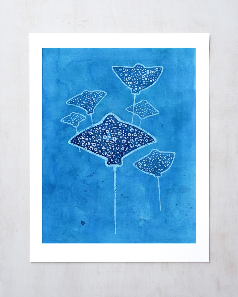 May include: A watercolor painting of five stingrays swimming in a blue ocean. The stingrays are white with black spots and have long tails.