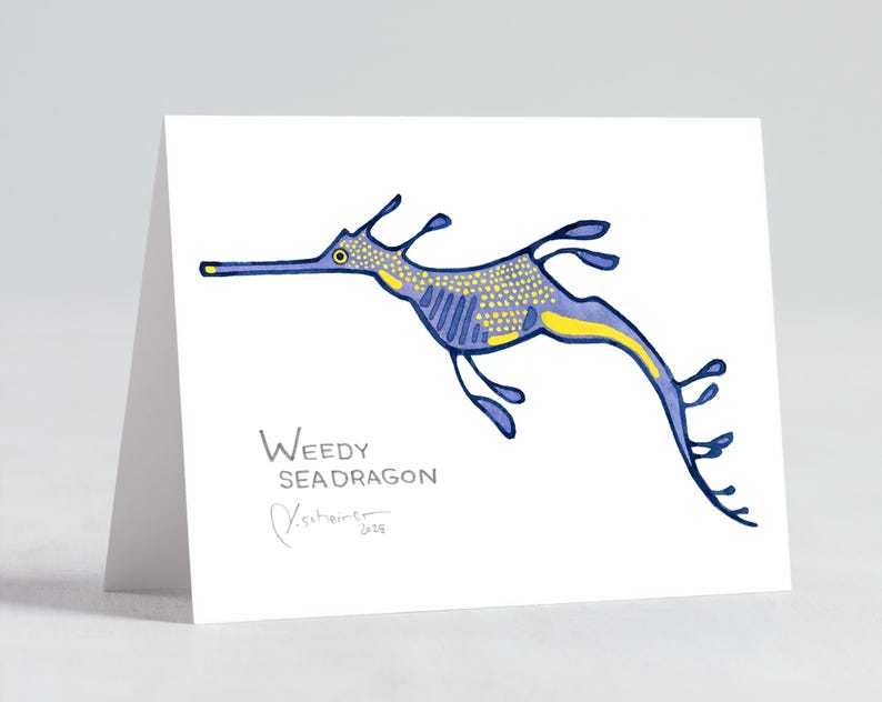 May include: A folded white greeting card featuring a blue and yellow illustration of a weedy seadragon. The seadragon has a long snout and flowing fins. The words "Weedy Seadragon" are printed below the illustration, along with an artist's signature.