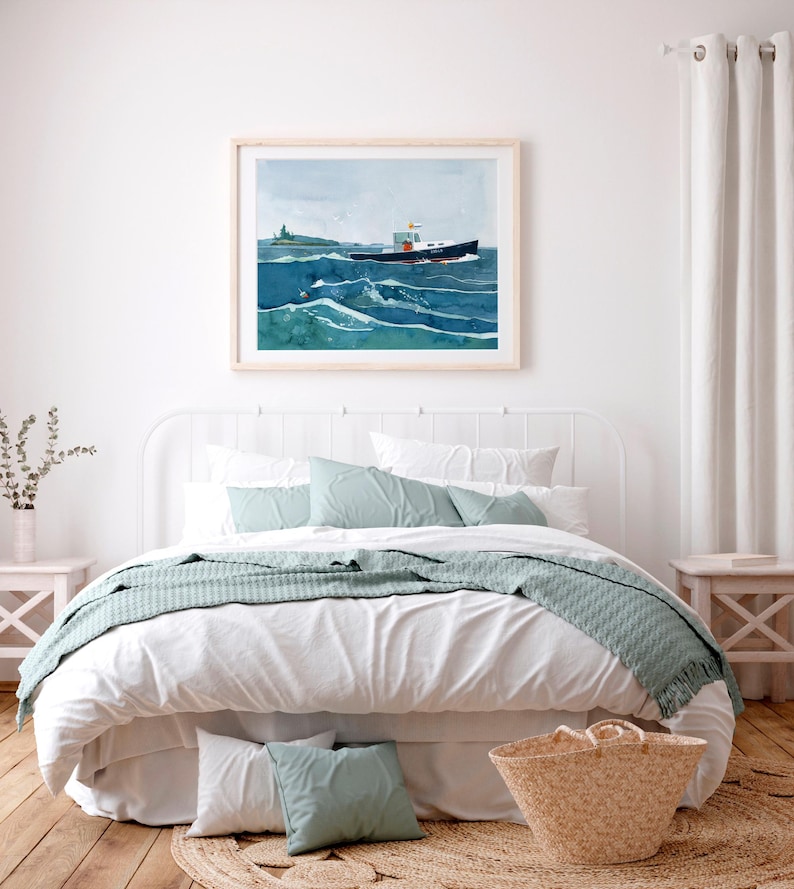 May include: A white bed with a white headboard and a white duvet cover. A blue blanket is draped over the foot of the bed. There are two blue pillows on the bed and a wicker basket on the floor next to the bed. A framed watercolor painting of a boat on the ocean hangs above the bed.