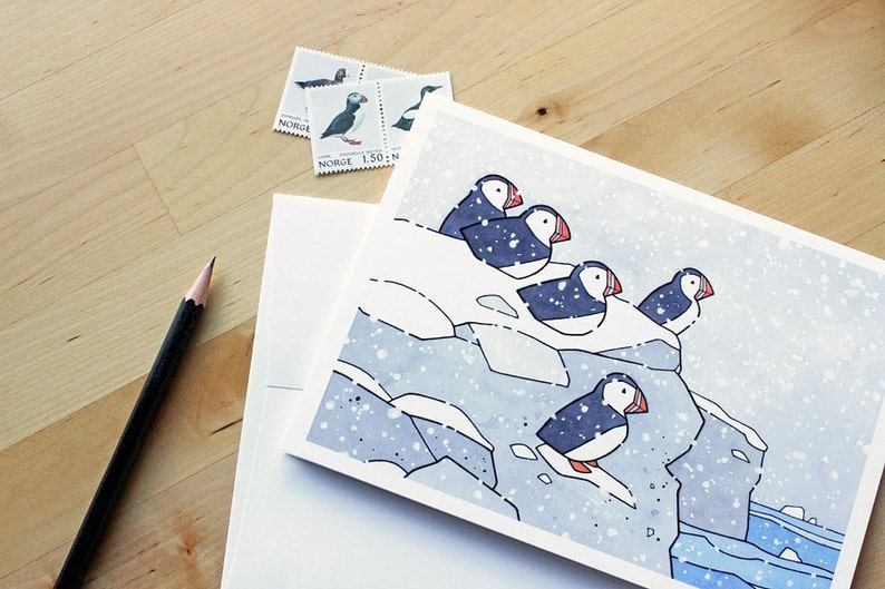 May include: A watercolor illustration of a group of puffins perched on a snowy cliff. The birds are facing different directions, with their beaks open and their wings folded. The background is a light blue color, with a few white dots representing snow.