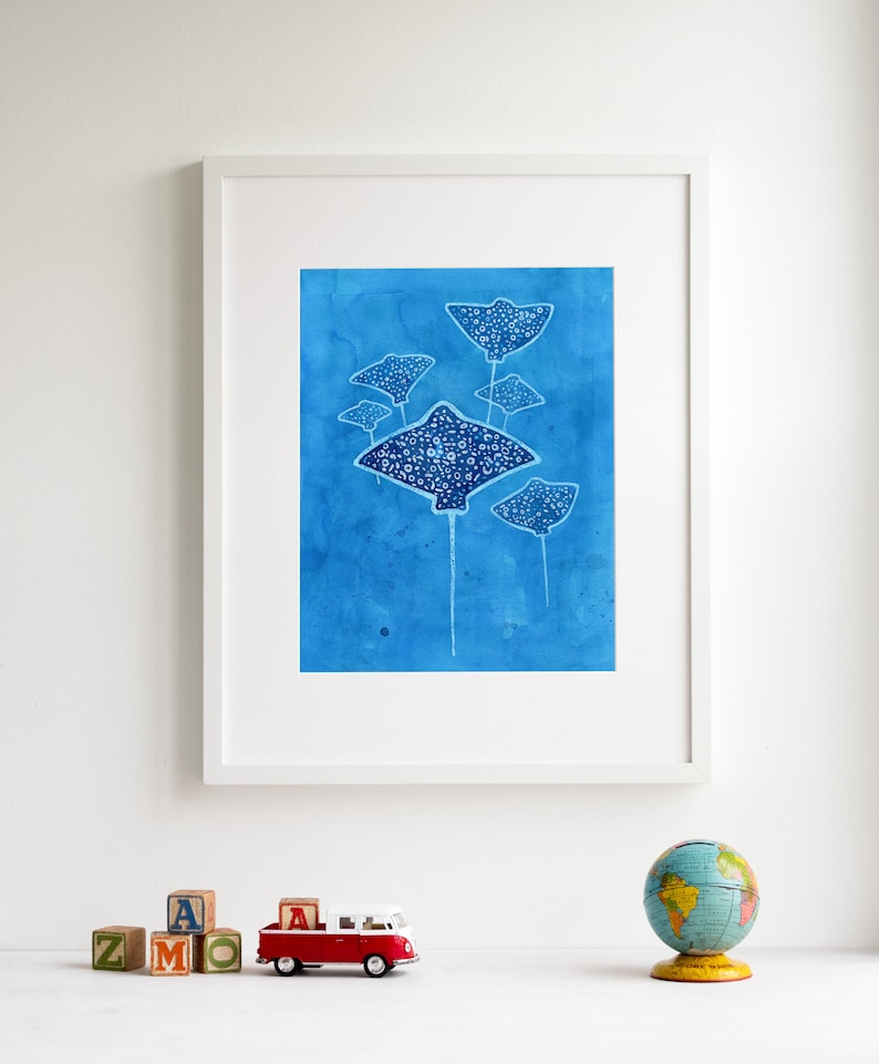 May include: A framed print of a watercolor painting featuring five blue stingrays with white spots on a blue background.