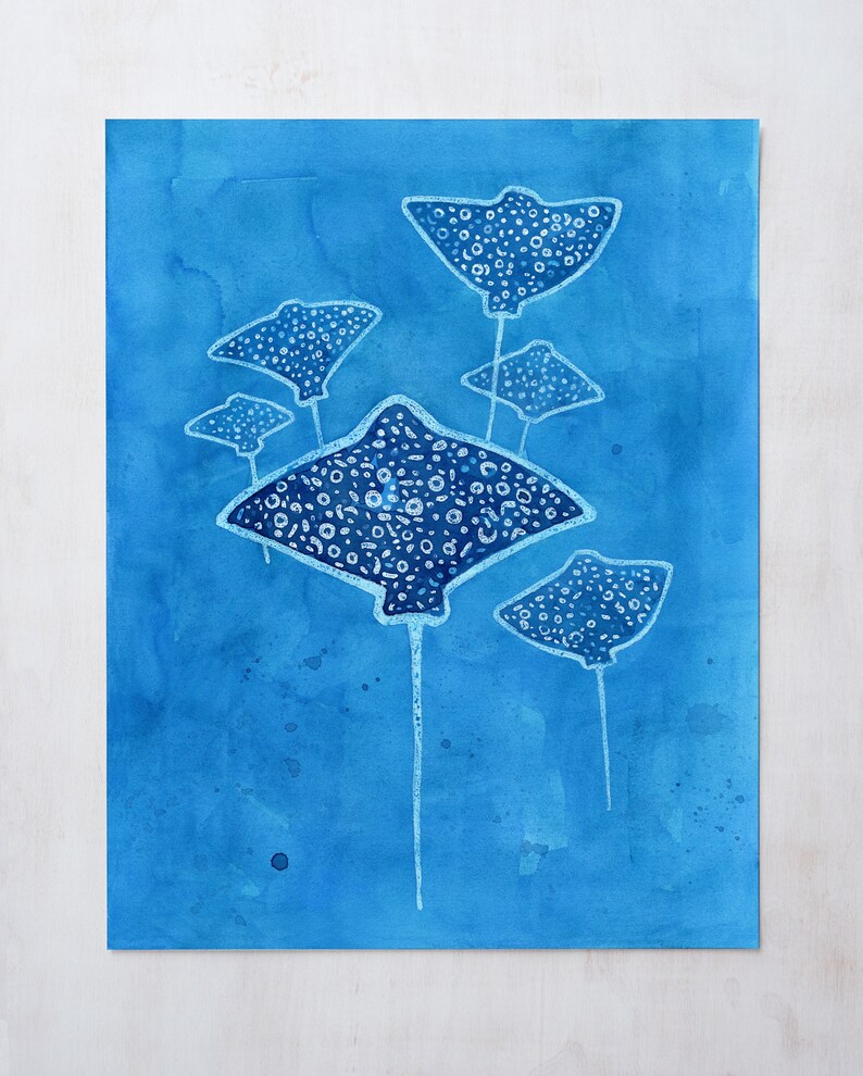 May include: A watercolor painting of five stingrays swimming in a blue ocean. The stingrays are white with black spots and have long tails.