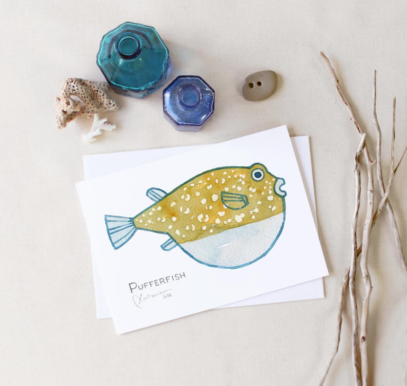 May include: Watercolor illustration of a pufferfish with yellow and white spots, blue fins, and a white belly. The artwork is on a white card with the word "Pufferfish" and artist's signature. Decorative blue glass bottles and a small stone are also in the image.