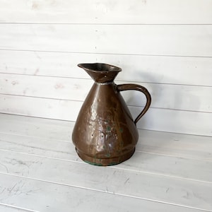 May include: A vintage copper jug with a hammered finish. The jug has a wide mouth and a handle. It is a rustic and charming piece.