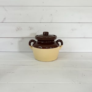 Puede incluir: Un tarro de cerámica de dos tonos con tapa. El tarro es de color beige claro en la parte inferior y marrón oscuro en la parte superior, incluida la tapa. Tiene dos asas pequeñas a cada lado. Ideal para la cocina.