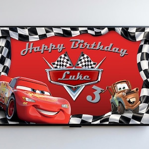 May include: A framed birthday banner featuring Lightning McQueen and Mater from the Cars movie. The banner has a red background with the words "Happy Birthday Luke" and the number 3. Checkered flags and a checkered border complete the design.