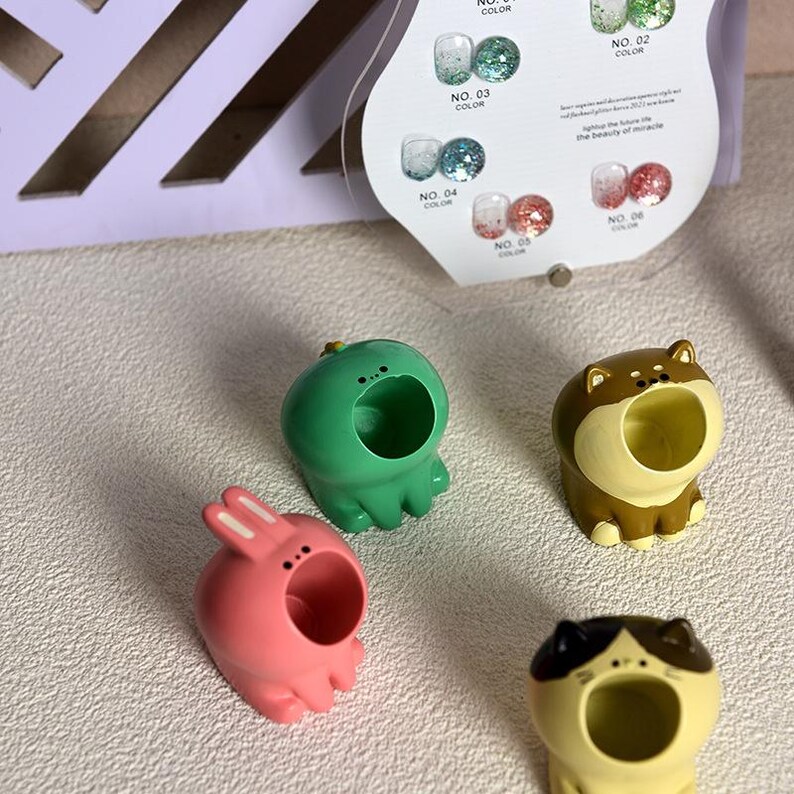 May include: Four colorful animal-shaped fingertip ring holders. The holders are a green frog, a pink bunny, a brown dog, and a yellow cat. Each holder has a large open mouth to hold rings.