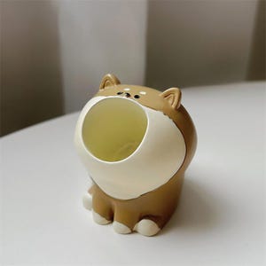 May include: A brown and white ceramic dog figurine with an open mouth, designed as a small planter or holder.