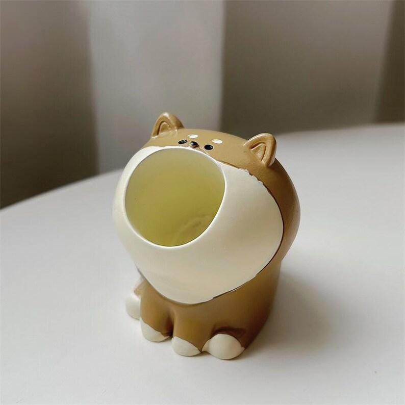 May include: A brown and white ceramic dog figurine with an open mouth, designed as a small planter or holder.