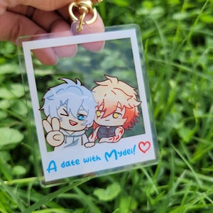 May include: Clear acrylic keychain featuring a cartoon image of two anime characters. One character has blue hair and is flashing a peace sign. The other has orange hair. The text "A date with Mydei!" is printed below the image.