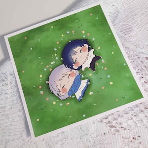 May include: A square print featuring two anime-style characters lying on a green field scattered with small flowers. One character has blue hair and the other has silver hair. The artwork has a soft, pastel color palette.