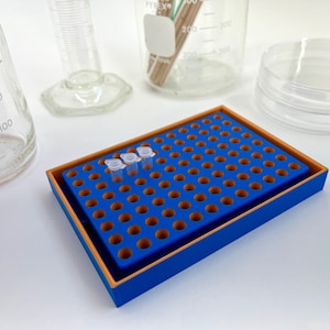 May include: A blue and orange plastic rack with 96 wells, designed to hold small test tubes. Three clear plastic test tubes are placed in the rack.