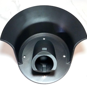 Puede incluir: Estación de carga negra impresa en 3D para vehículo eléctrico. La estación tiene una base circular con un puerto de carga central y una parte superior curvada. El diseño es moderno y funcional, con un acabado mate.