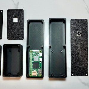 May include: A set of black plastic components for a Raspberry Pi project. The components include a case, a camera module, and a variety of other parts.