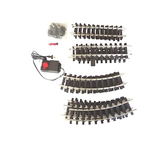 May include: A model railway set featuring black track sections with silver rails, and a power supply unit. The set includes straight and curved track pieces, connectors, and a power controller with a red dial. The components are arranged on a white surface.