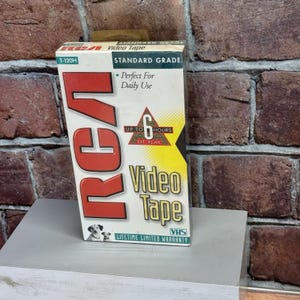 May include: RCA T-120H VHS video tape box. The box is white with red and black text, including "RCA" in large letters. It features the text "Standard Grade" and "Up to 6 Hours of Play". The box has a picture of two dogs and the text "Lifetime Limited Warranty".
