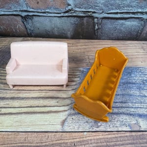 May include: A miniature pink sofa and an orange cradle. The sofa has a rectangular shape with armrests and short legs. The cradle is a rocking style with a curved base and vertical slats.
