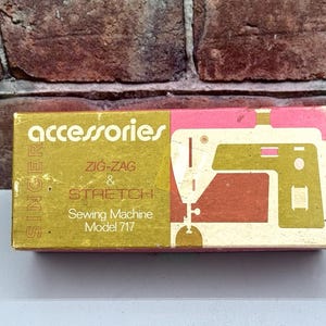 May include: A vintage Singer sewing machine accessories box. The box is gold and pink with the word "accessories" in white. It features a sewing machine graphic and text that reads "Zig-Zag & Stretch Sewing Machine Model 717".