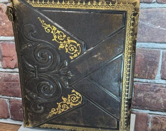 Puede incluir: Un libro antiguo de cuero marrón oscuro con detalles dorados de filigrana. La cubierta presenta diseños florales en relieve y un cierre de metal. Los bordes están adornados con detalles dorados, y el libro parece envejecido.