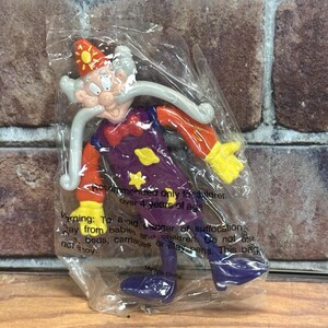 以下が含まれることがあります： プラスチックの袋に入った漫画の魔法使いのフィギュア。魔法使いは赤い帽子、オレンジ色の袖、黄色の星が付いた紫色のチュニック、青い靴を履いています。中国製。