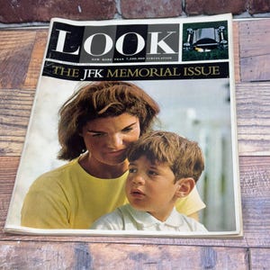 Pode incluir: Uma edição vintage da revista Look com uma capa com uma mulher e um menino. A revista diz "LOOK" e "THE JFK MEMORIAL ISSUE". A mulher usa uma camisa amarela e o menino usa uma camisa branca.