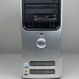 Op de afbeelding: Een zilverkleurige Dell Dimension E520 desktop computer tower met een zwart voorpaneel voorzien van een dvd-station, een geheugenkaartlezer, twee USB-poorten en audio-aansluitingen. De voorzijde bevat een rond Dell-logo en ventilatieroosters.
