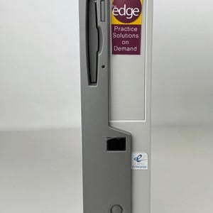 May include: A vertical computer tower in light gray and dark gray featuring a floppy disk drive slot, a power button, and several ports. A sticker on the front displays the text: the edge Practice Solutions on Demand, and a smaller CAESY Enterprise logo.