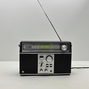 May include: A black and silver portable radio with a long, thin, extendable metal aerial. The front panel features a tuning dial, a green label reading Stereo/2 Speakers, the brand name LLOYDS, and various control knobs and switches.