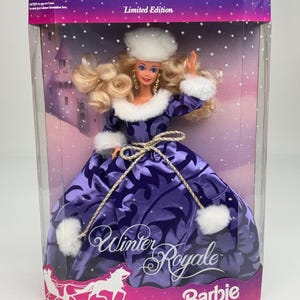 Puede incluir: Una muñeca rubia con un vestido de satén morado con un patrón de hojas de color morado oscuro, ribete de piel sintética blanca en el cuello, puños y gorro, y un cinturón de cordón dorado. El empaque dice Limited Edition, Winter Royale y Barbie.