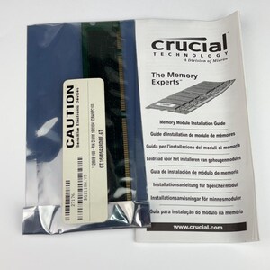 May include: A Crucial Technology memory module in a static-shielding bag with a caution label reading 128MB 168-PIN DIMM 16MX64 SDRAM PC100 CT16M64S8D8E.4T, accompanied by a white paper Memory Module Installation Guide with multilingual text.