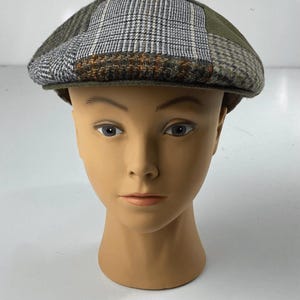 May include: A flat cap featuring a patchwork design of various wool-like fabrics in shades of olive green, grey, brown, and white. The cap displays multiple patterns including houndstooth, plaid, and solid panels, with a structured brim.