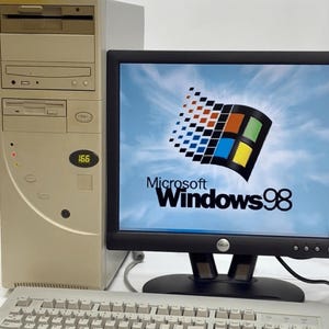 Puede incluir: Una torre de computadora de escritorio beige con disquetera y unidad de CD-ROM, junto a un monitor Dell negro que muestra el logotipo de Microsoft Windows 98 sobre un fondo de cielo azul, y un teclado QWERTY beige en primer plano.