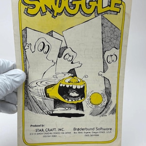 May include: A rectangular paper flyer titled SNOGGLE in bold yellow letters. The illustration features three white ghost-like figures and a yellow creature with a wide mouth. Text includes Produced by: STAR CRAFT, INC. and Brøderbund Software.