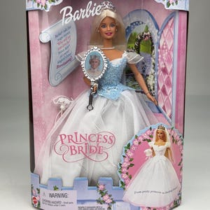 Puede incluir: Una muñeca Barbie Princess Bride en su empaque original. La muñeca tiene cabello rubio, una tiara plateada y un vestido azul y blanco. Sostiene un espejo de mano con una imagen de Ken. La caja incluye texto como Barbie, Princess Bride y una advertencia.