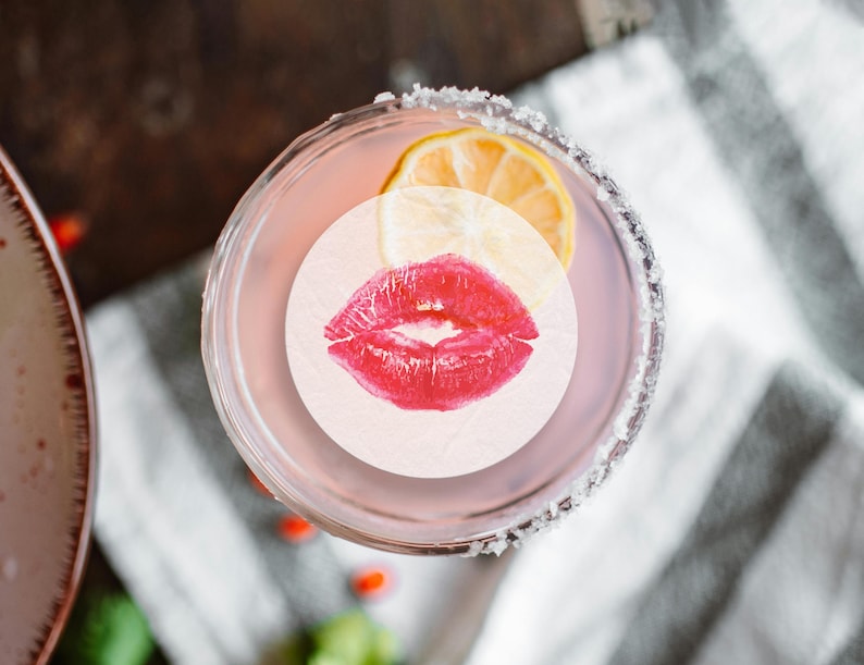May include: A pink cocktail with a lemon wedge and a red lipstick kiss on a white circle sticker.